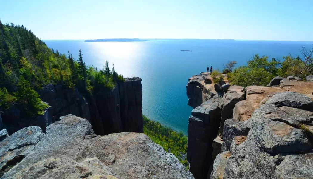 Deux randonneurs se tiennent au bord d'une falaise rocheuse surplombant le lac Supérieur, au sommet du sentier de randonnée du Sleeping Giant.