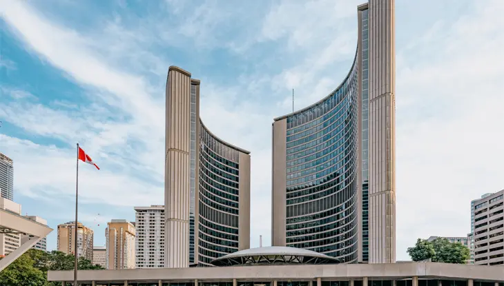 Toronto City Hall with Canadian flag under partly cloudy sky.