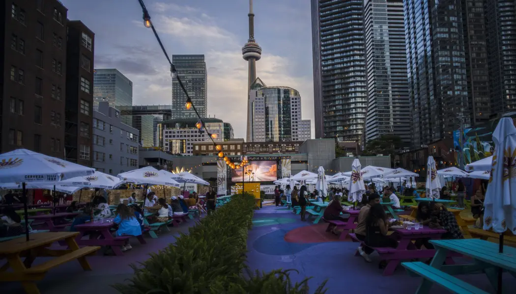 Der CN Tower ist im Hintergrund einer Szene zu sehen, in der Menschen auf einer Terrasse plaudern und entspannen.