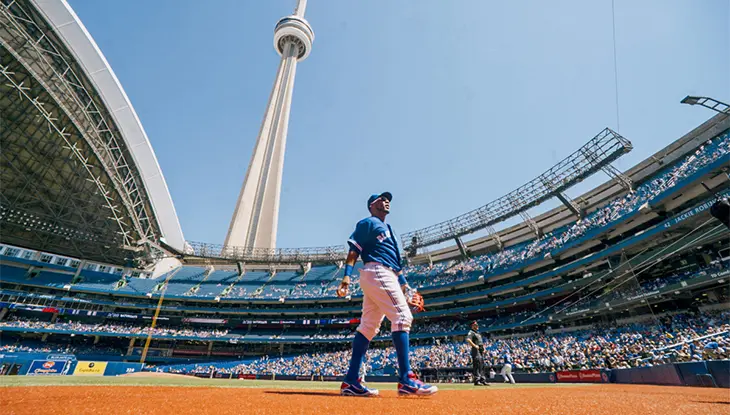 Joueur de baseball marchant sur le terrain au Centre Rogers, avec la Tour CN en arrière-plan.