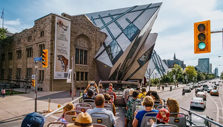 Un autobús turístico descapotable pasa junto al Museo Real de Ontario, con su fachada angular de cristal.