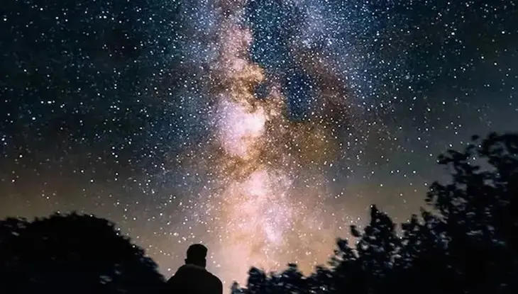 Silhouette d'une personne levant les yeux vers un ciel étoilé et coloré.