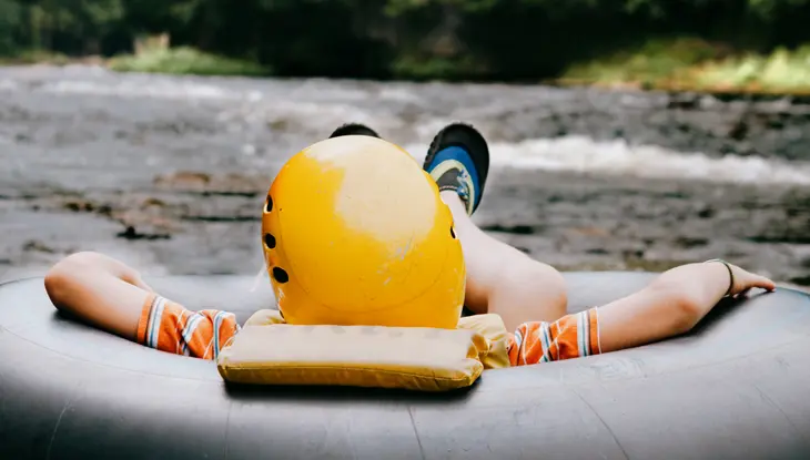 黄色いヘルメットをかぶった少年が、大きな黒いインナーチューブに乗って、穏やかなエローラ渓谷の急流を下っています。