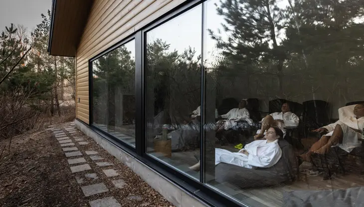 Plusieurs personnes portant un peignoir blanc se détendent dans une salle avec vue sur la forêt au centre de bien-être Vettä Spa.