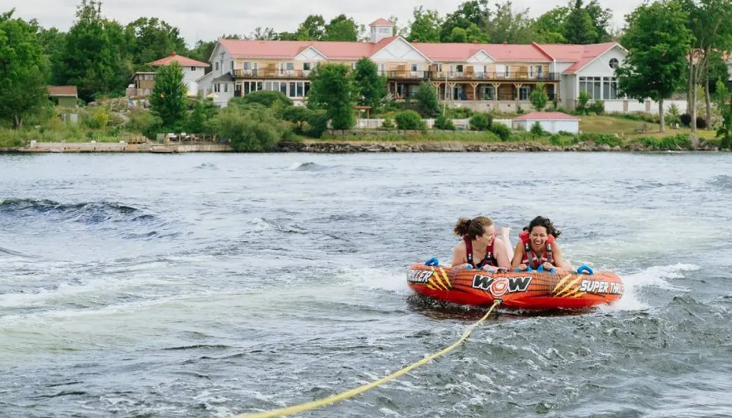 Deux jeunes femmes s’amusant dans une chambre à air tirée par un bateau sur un lac de la région des Kawarthas, en Ontario.