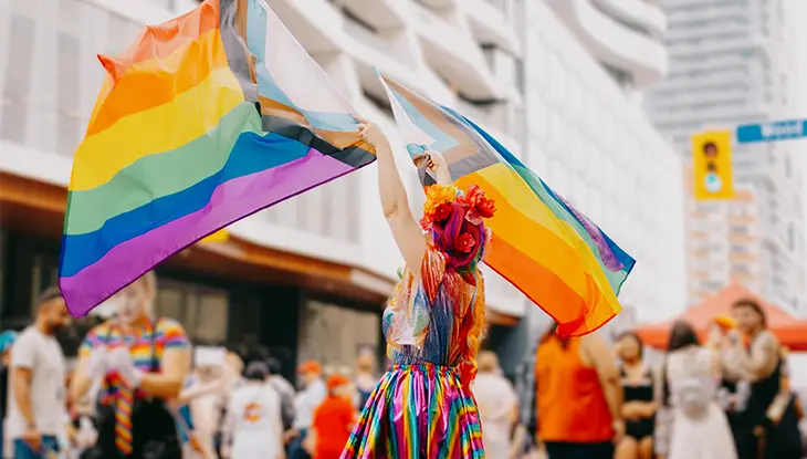 Participant au défilé portant des drapeaux arc-en-ciel pendant les célébrations de la Fierté à Toronto.
