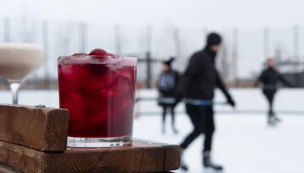 Dos cócteles se sientan en una barra de madera junto a personas que patinan sobre hielo y juegan al hockey en la pista de Wayne Gretzky Estates.