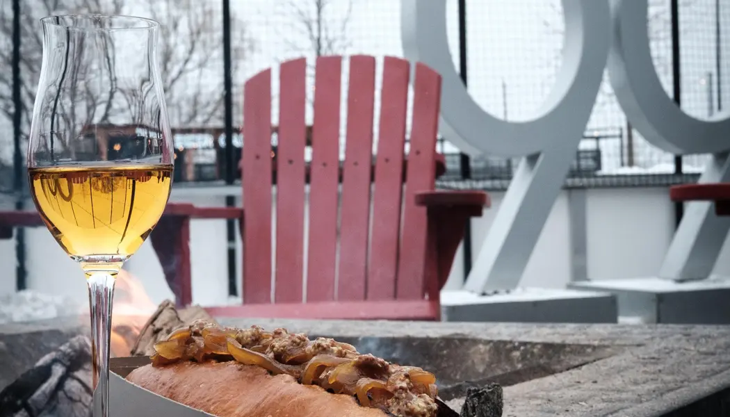 A glass of white wine is set down beside an outdoor fire pit with an ice rink and the number 99 in the background at Gretzky Estates Winery.