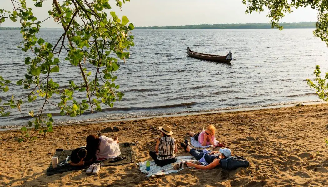 Cinq personnes se prélassent sur des couvertures de plage étendues sur le sable de la plage de Westboro à Ottawa.