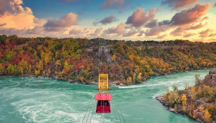 Téléphérique rouge traversant la rivière Niagara avec, en arrière-plan, les magnifiques couleurs d’automne.