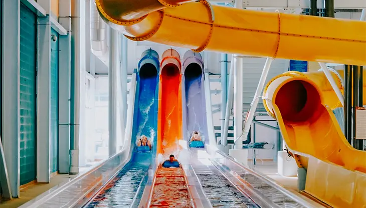 Des personnes dévalent en bouée un ensemble de trois toboggans aquatiques colorés dans un parc aquatique intérieur.