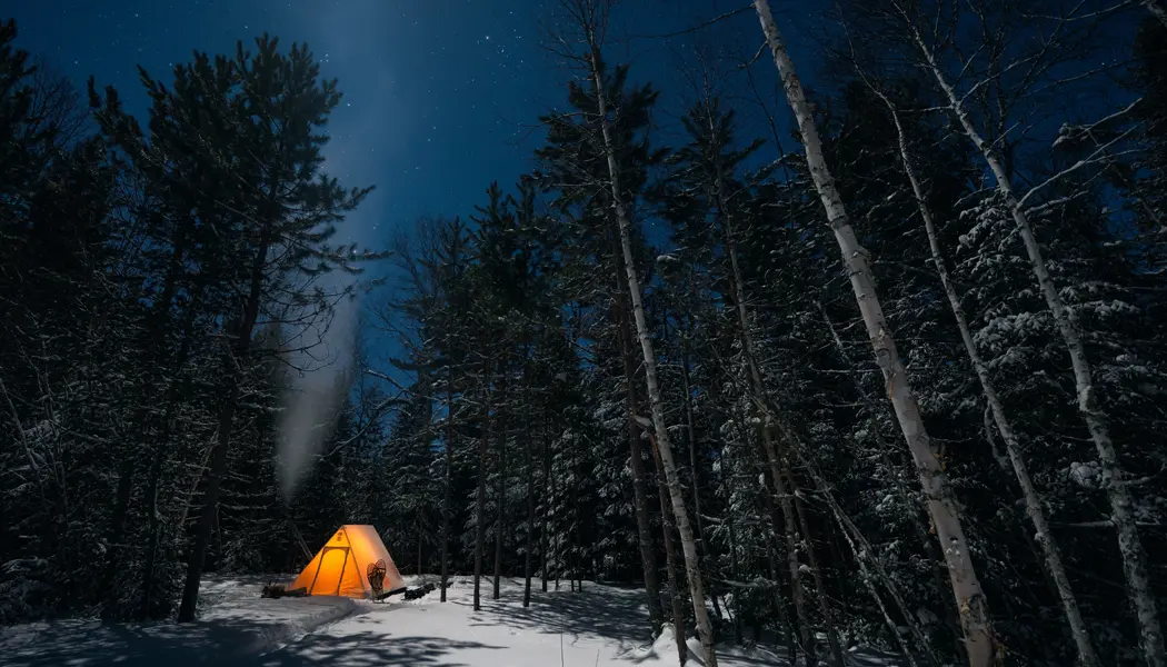 Une tente est illuminée dans la noirceur durant un voyage de camping d’hiver dans la forêt.