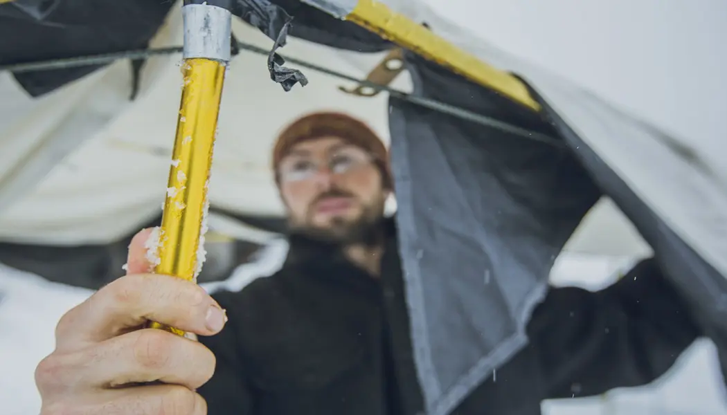 Un homme fixe un poteau au sommet d'une tente pour installer son campement d'hiver.